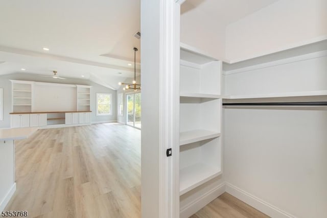 spacious closet with light wood finished floors, vaulted ceiling, and ceiling fan with notable chandelier