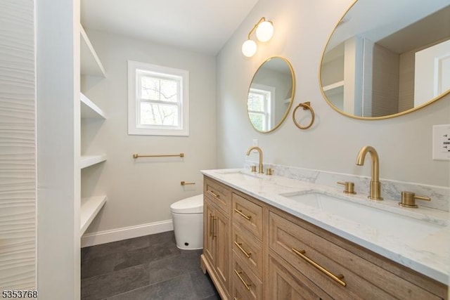 bathroom with toilet, double vanity, a sink, and baseboards
