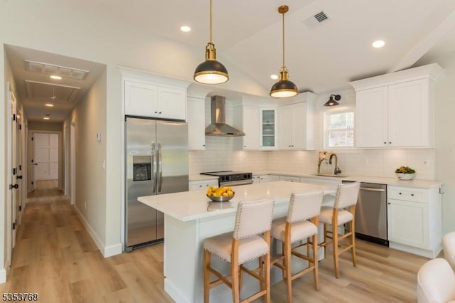 kitchen with a sink, visible vents, appliances with stainless steel finishes, and wall chimney range hood