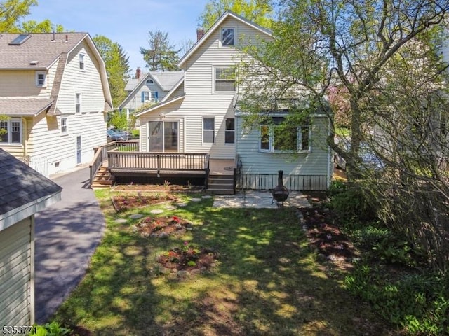 back of property featuring a wooden deck, a chimney, and a lawn