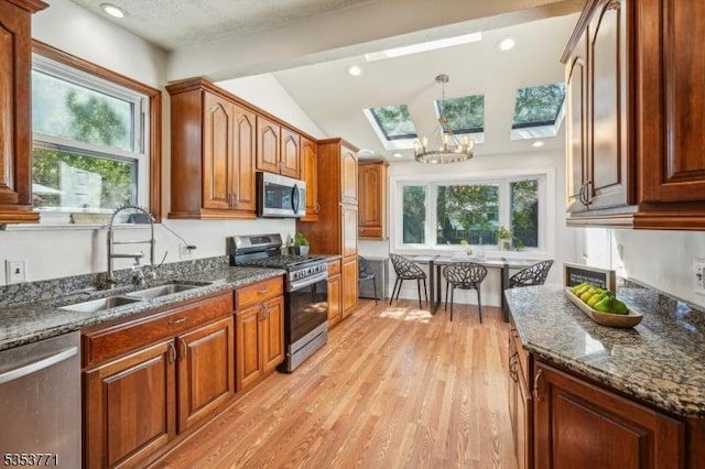 kitchen with stainless steel appliances, a sink, a skylight, light wood-style floors, and lofted ceiling