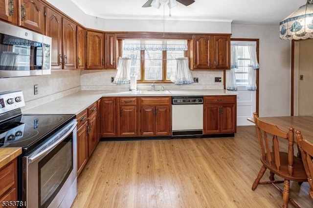 kitchen with light wood finished floors, brown cabinetry, stainless steel appliances, and light countertops