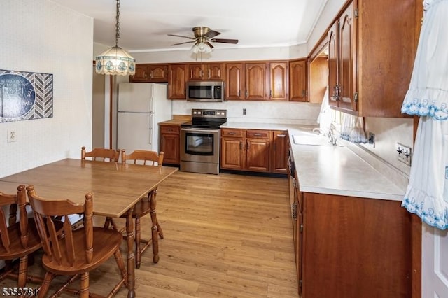 kitchen with light wood finished floors, brown cabinets, a sink, a ceiling fan, and appliances with stainless steel finishes