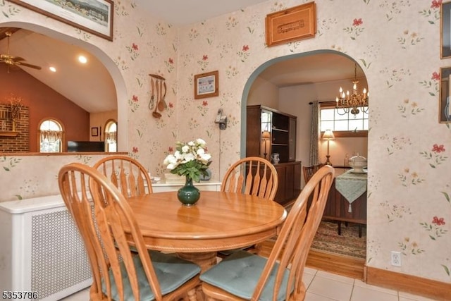 dining room with light tile patterned floors, arched walkways, ceiling fan with notable chandelier, and wallpapered walls