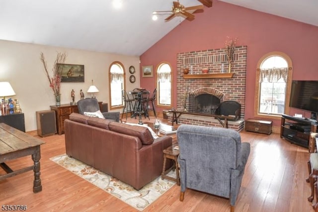 living area with a brick fireplace, a ceiling fan, a healthy amount of sunlight, and wood finished floors