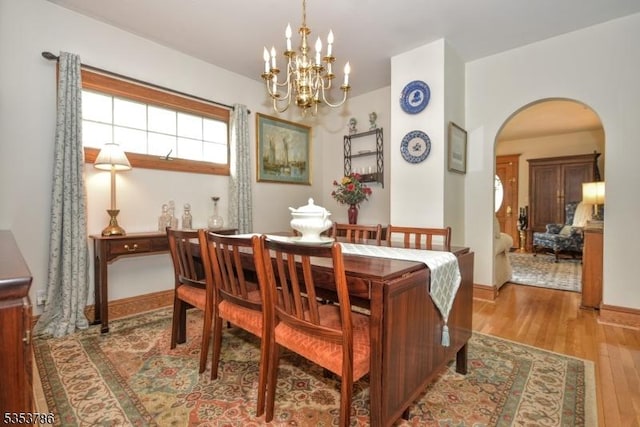 dining area with arched walkways, baseboards, an inviting chandelier, and wood finished floors
