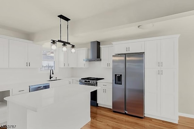 kitchen with a sink, stainless steel appliances, wall chimney exhaust hood, light countertops, and white cabinets