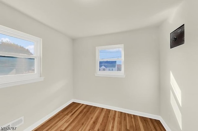 empty room featuring visible vents, baseboards, wood finished floors, and a healthy amount of sunlight
