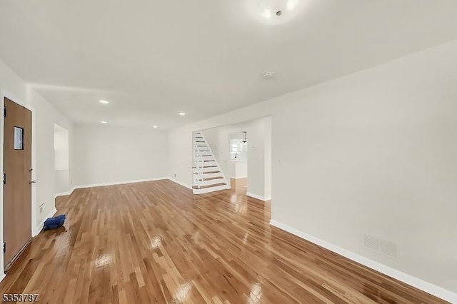 unfurnished living room featuring light wood-style flooring, visible vents, baseboards, recessed lighting, and stairs