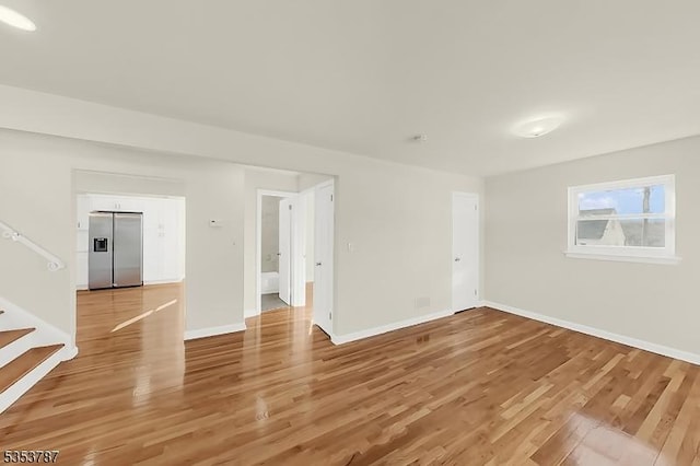 empty room featuring baseboards, stairs, and light wood finished floors