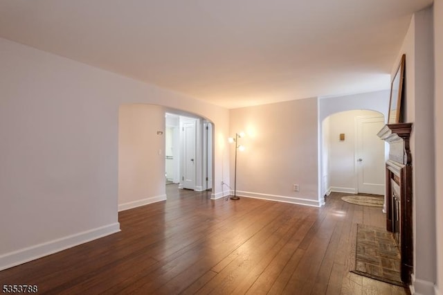 unfurnished living room with arched walkways, baseboards, and dark wood-style floors