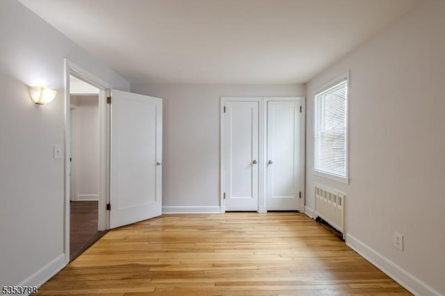 unfurnished bedroom featuring radiator, baseboards, and light wood finished floors