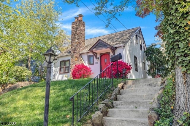 view of front facade featuring a shingled roof, stucco siding, a chimney, and a front yard