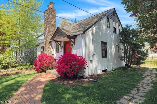 view of front of property with roof with shingles, stucco siding, a front yard, and a chimney
