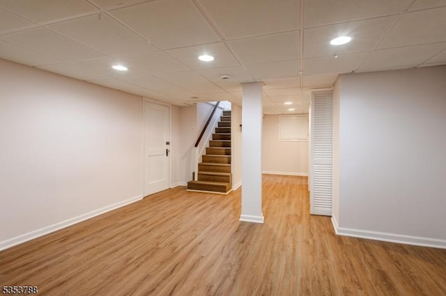 finished below grade area with a paneled ceiling, light wood-style flooring, recessed lighting, baseboards, and stairway