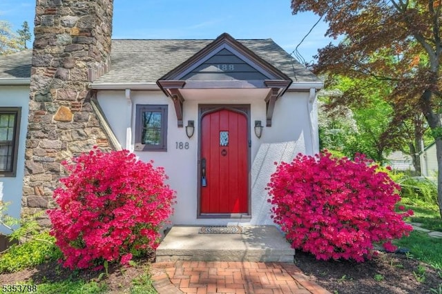 entrance to property featuring a shingled roof, a chimney, and stucco siding