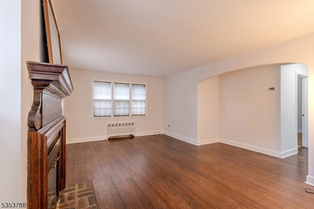 unfurnished living room with a fireplace, baseboards, radiator heating unit, arched walkways, and dark wood finished floors