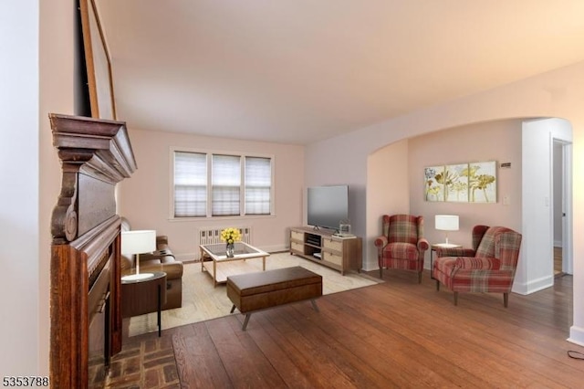 living area with arched walkways, radiator heating unit, and wood finished floors
