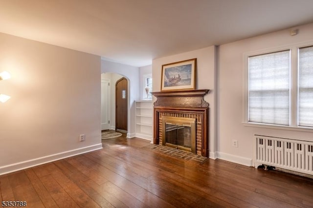 unfurnished living room with baseboards, arched walkways, radiator, and hardwood / wood-style floors