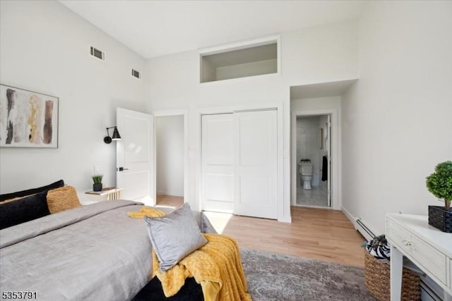 bedroom featuring a towering ceiling, baseboard heating, wood finished floors, and visible vents