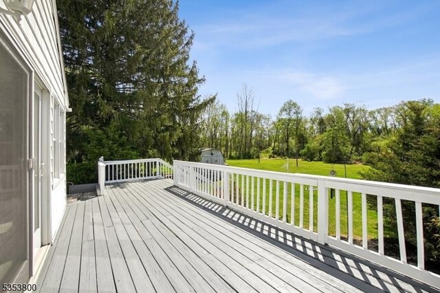 deck featuring a shed, a lawn, view of wooded area, and an outdoor structure