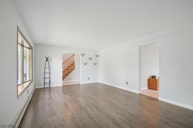 unfurnished living room with arched walkways, dark wood-style floors, a baseboard heating unit, and baseboards