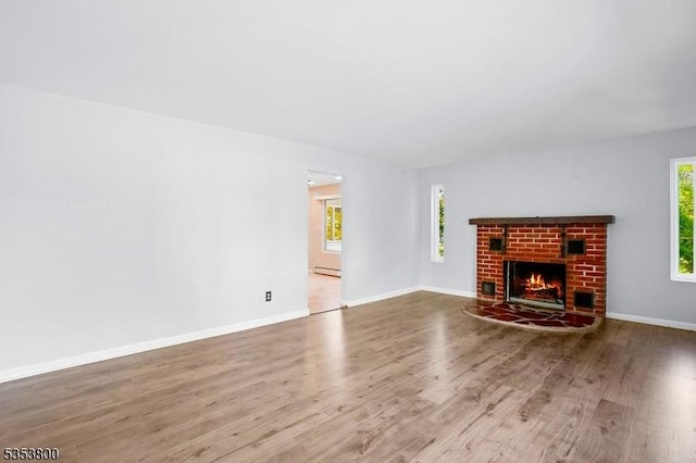 unfurnished living room with a baseboard heating unit, wood finished floors, baseboards, and a brick fireplace
