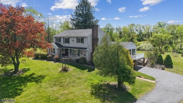 view of front facade with a chimney, a front lawn, asphalt driveway, and view of wooded area