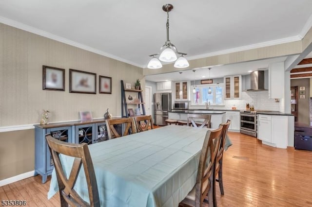 dining area featuring light wood-type flooring, ornamental molding, and baseboards