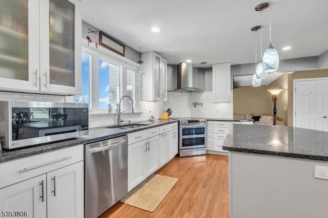 kitchen featuring wall chimney range hood, white cabinets, a sink, stainless steel appliances, and decorative backsplash
