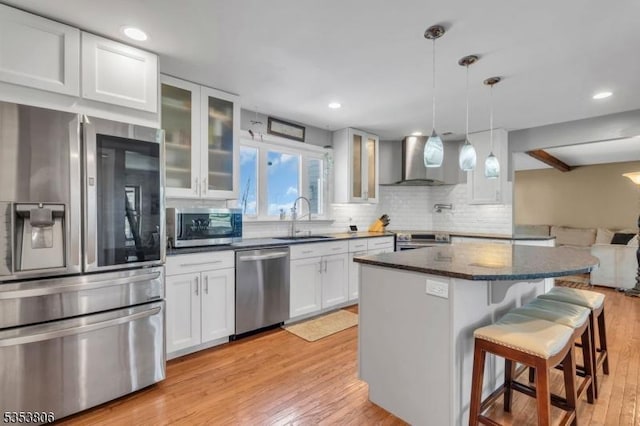 kitchen featuring wall chimney range hood, a kitchen bar, a sink, light wood-style floors, and stainless steel appliances