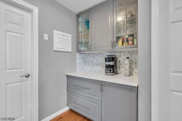 bar with baseboards, tasteful backsplash, a bar, and light wood finished floors