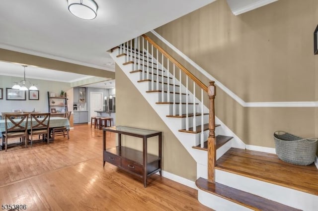 staircase with baseboards, an inviting chandelier, ornamental molding, and wood finished floors