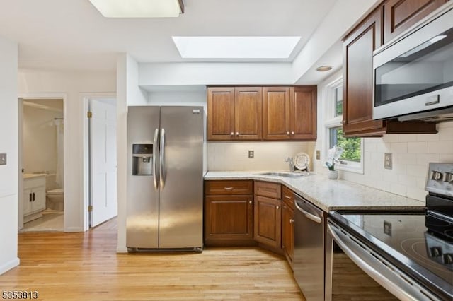 kitchen with light wood-style floors, tasteful backsplash, a sink, a skylight, and stainless steel appliances