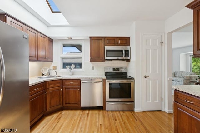 kitchen featuring light wood-type flooring, tasteful backsplash, a sink, appliances with stainless steel finishes, and a skylight
