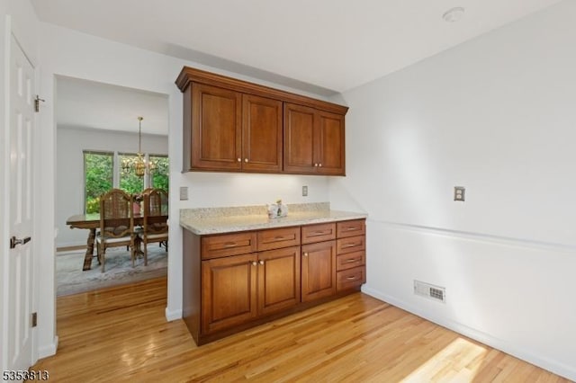 kitchen featuring an inviting chandelier, visible vents, light wood-type flooring, brown cabinets, and light stone counters