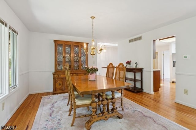 dining space with baseboards, light wood finished floors, a chandelier, and visible vents