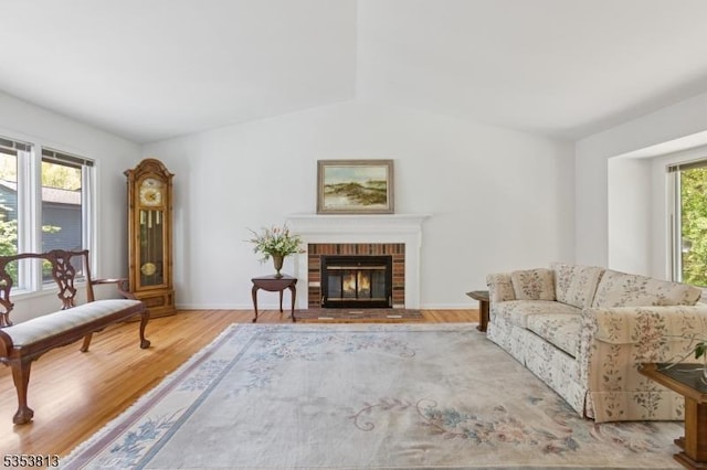living area with baseboards, a brick fireplace, and wood finished floors