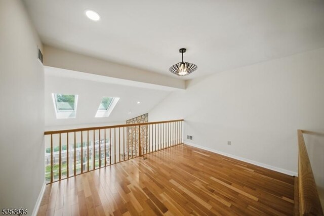additional living space featuring visible vents, baseboards, lofted ceiling with skylight, and wood finished floors