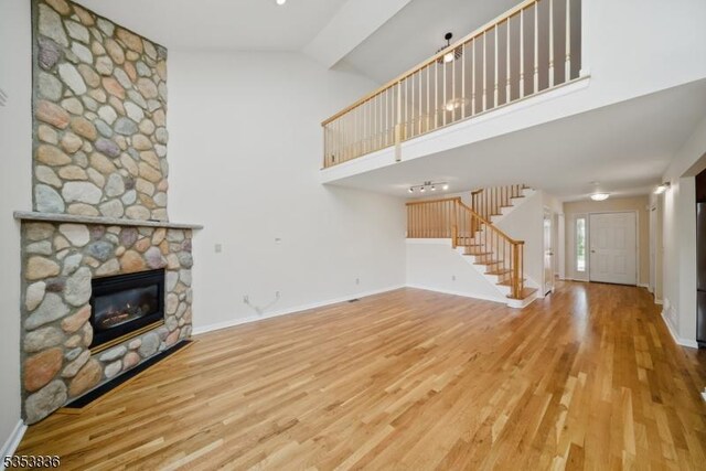 unfurnished living room with stairs, high vaulted ceiling, a stone fireplace, and wood finished floors