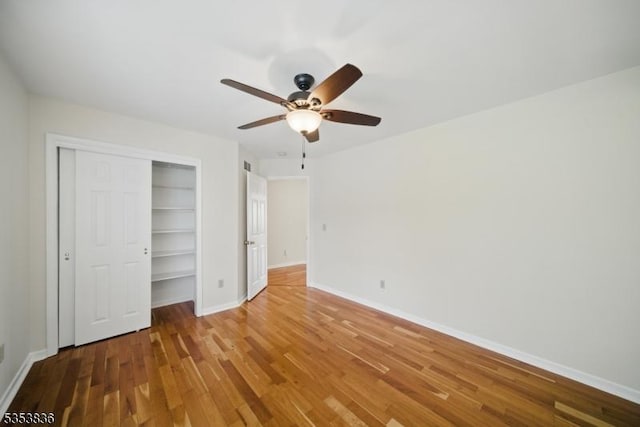 unfurnished bedroom featuring a ceiling fan, baseboards, wood finished floors, and a closet