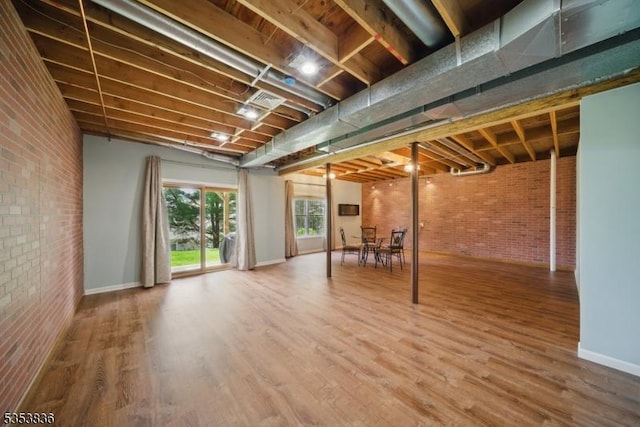 basement featuring baseboards, wood finished floors, brick wall, and visible vents