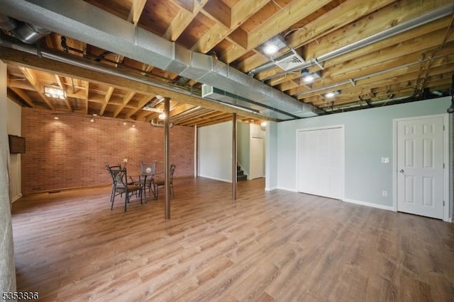 finished basement with brick wall, stairs, baseboards, wood finished floors, and visible vents