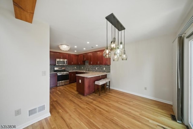 kitchen featuring visible vents, a peninsula, a breakfast bar, backsplash, and stainless steel appliances