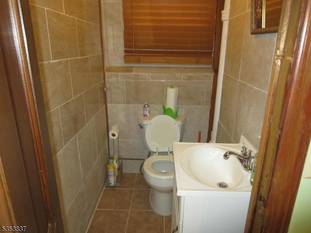 half bath with tile walls, tile patterned flooring, vanity, and toilet