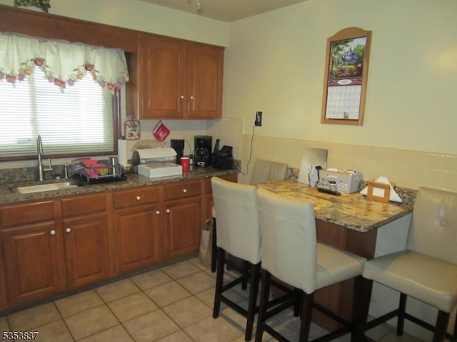 kitchen featuring brown cabinets, light tile patterned flooring, a breakfast bar, and a sink