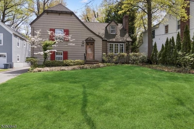 view of front of house with a shingled roof, a chimney, and a front yard