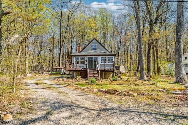 chalet / cabin with dirt driveway, a view of trees, a wooden deck, and stairway