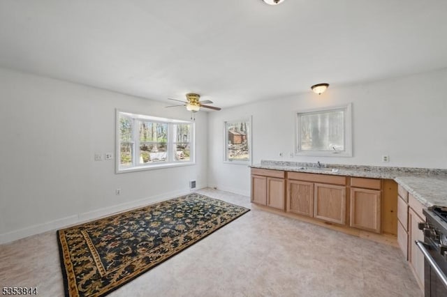 kitchen with ceiling fan, high end range, a sink, light stone counters, and baseboards