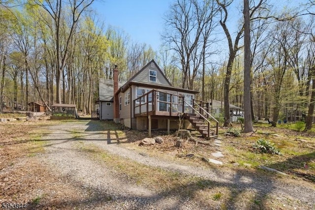 view of front of house with stairs, dirt driveway, a sunroom, and a chimney